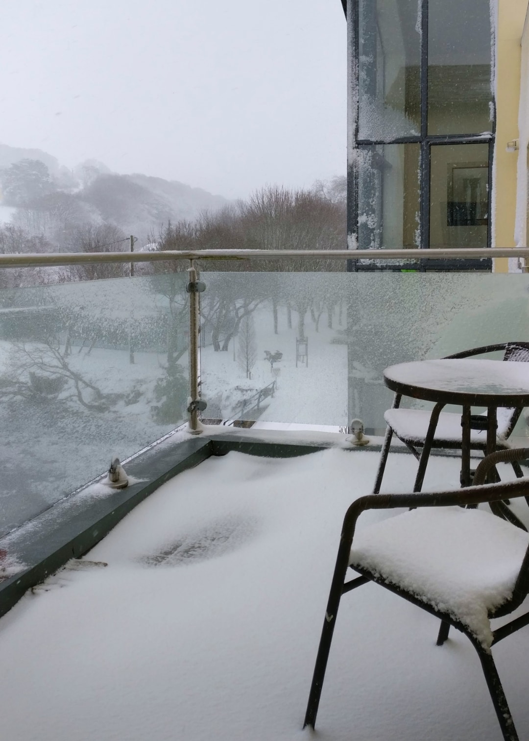 Apartment balcony with chairs and table covered in snow